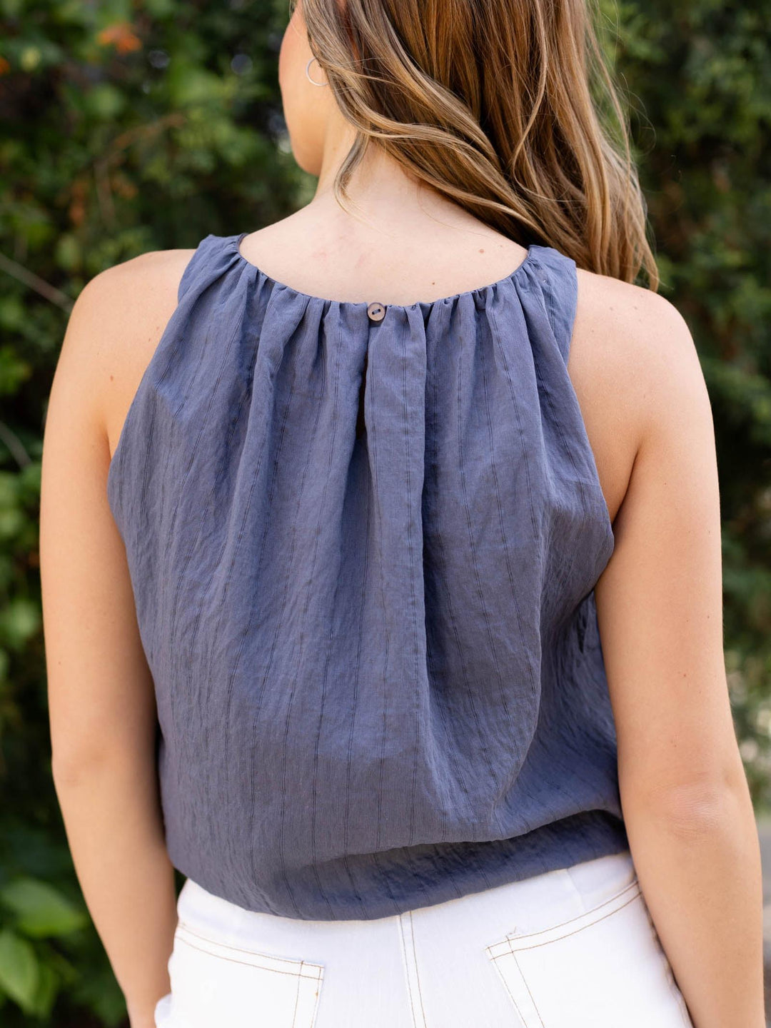 Woman wearing a navy bubble striped tank top with a button back closure, paired with white pants.