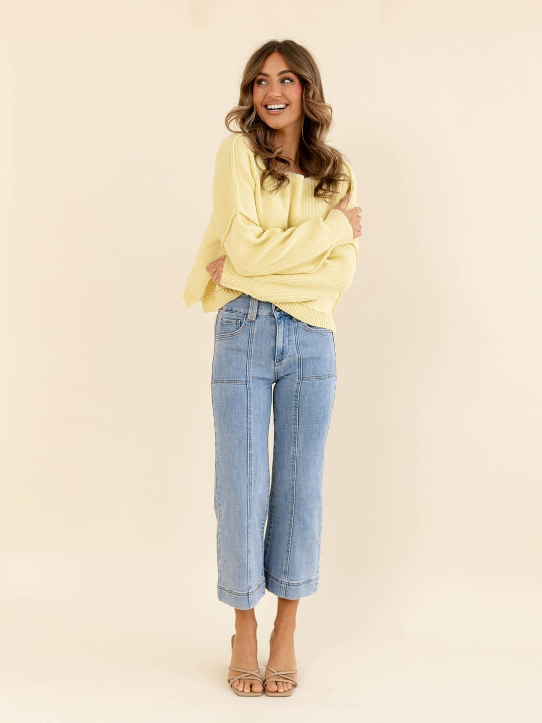 Woman wearing a yellow sweater and blue jeans on a beige background