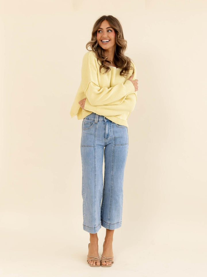 Woman wearing a yellow sweater and blue jeans on a beige background
