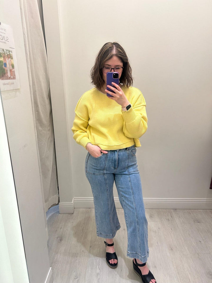 Person wearing a yellow sweater and blue jeans taking a mirror selfie.