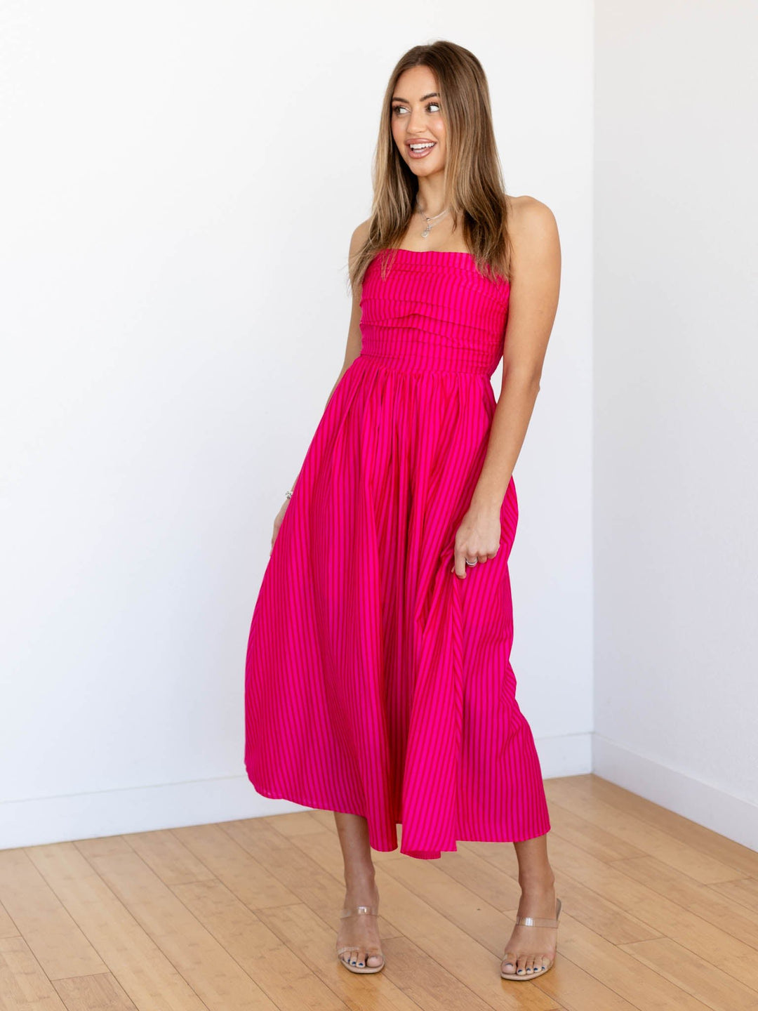 Woman wearing a bright pink dress standing against a white wall.