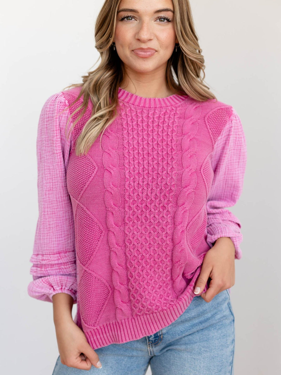 Woman wearing a pink cable knit sweater and blue jeans on a light background