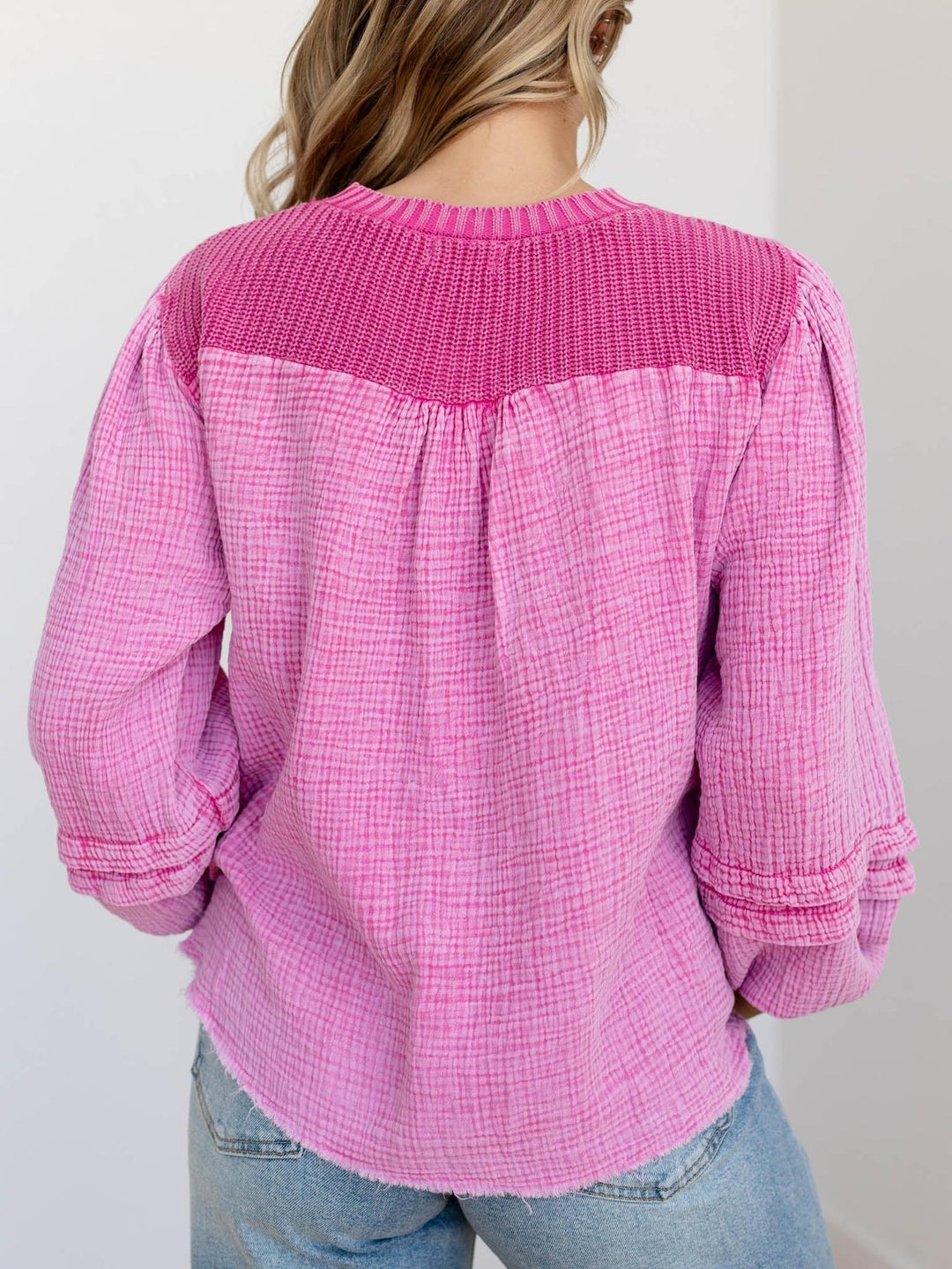Woman wearing a pink cable knit sweater and blue jeans on a light background