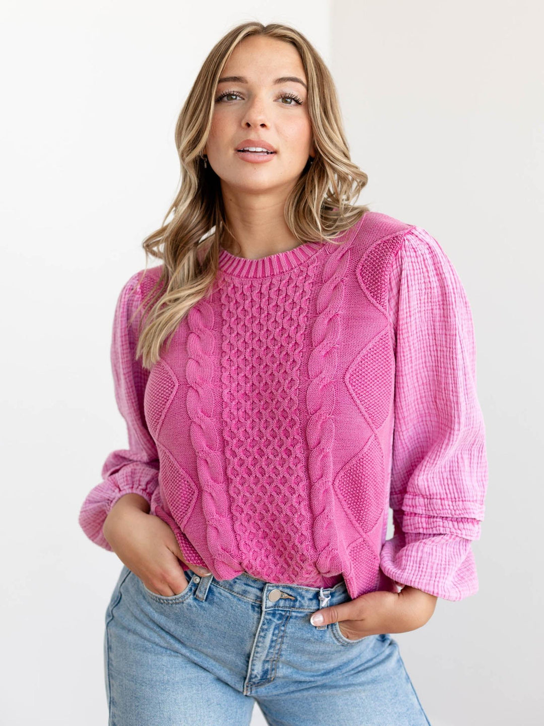 Woman wearing a pink cable knit sweater and blue jeans on a light background