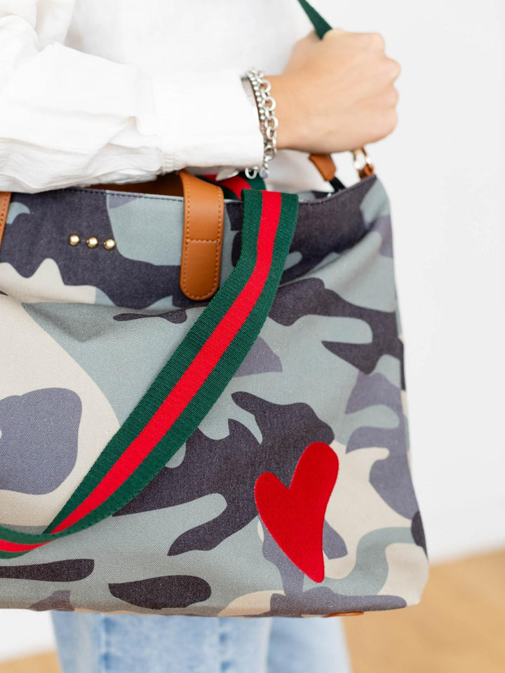 Camouflage bag with red heart and green and red strap held by a person.