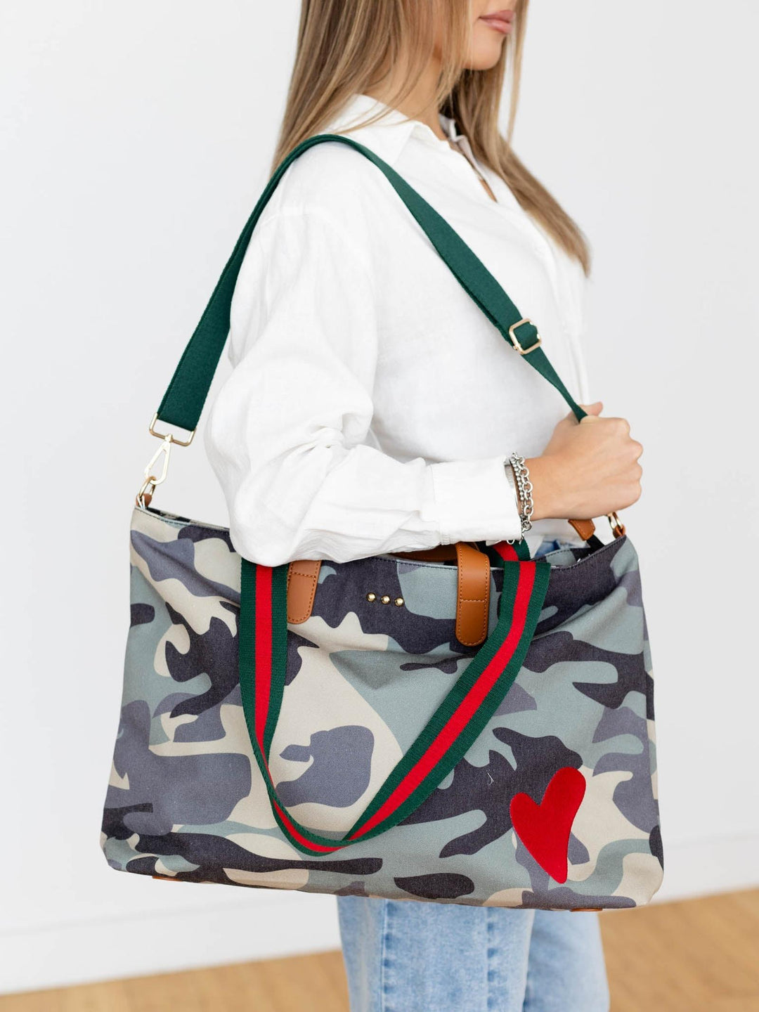 Person holding a camouflage tote bag with green straps and a red heart on a white background