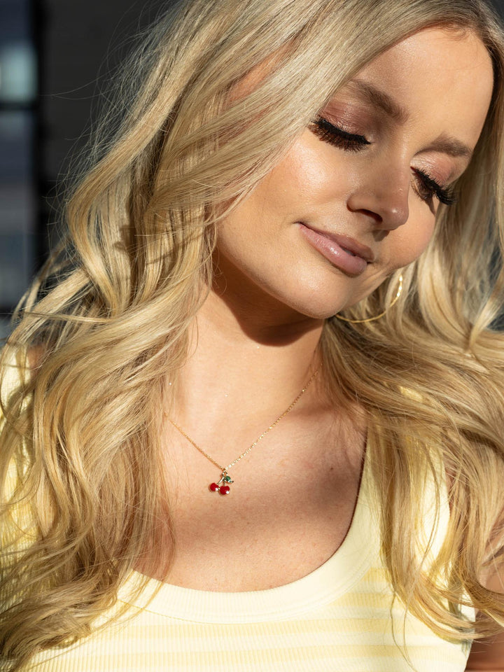 Woman with blonde hair wearing a necklace with red berries.