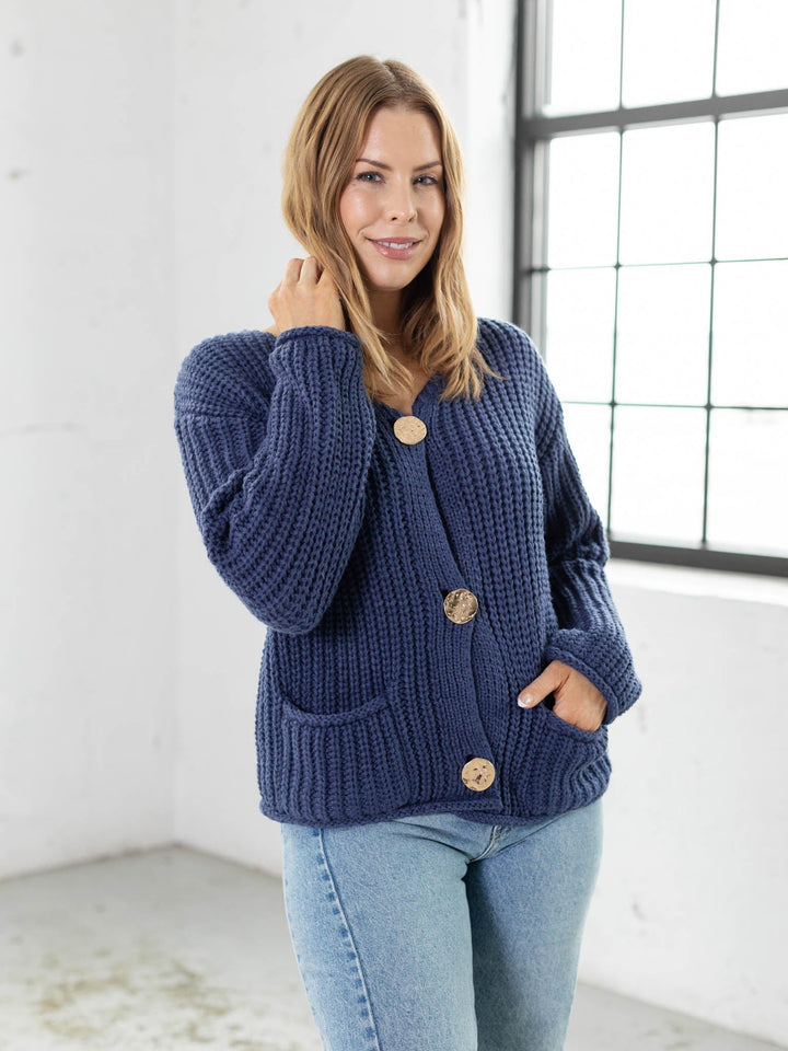 Woman wearing a blue cardigan with button details in a bright room.