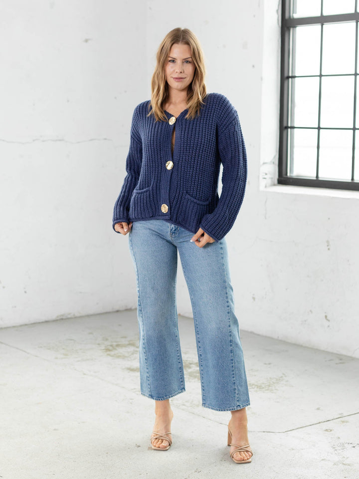 Woman wearing a blue cardigan and jeans in a white room