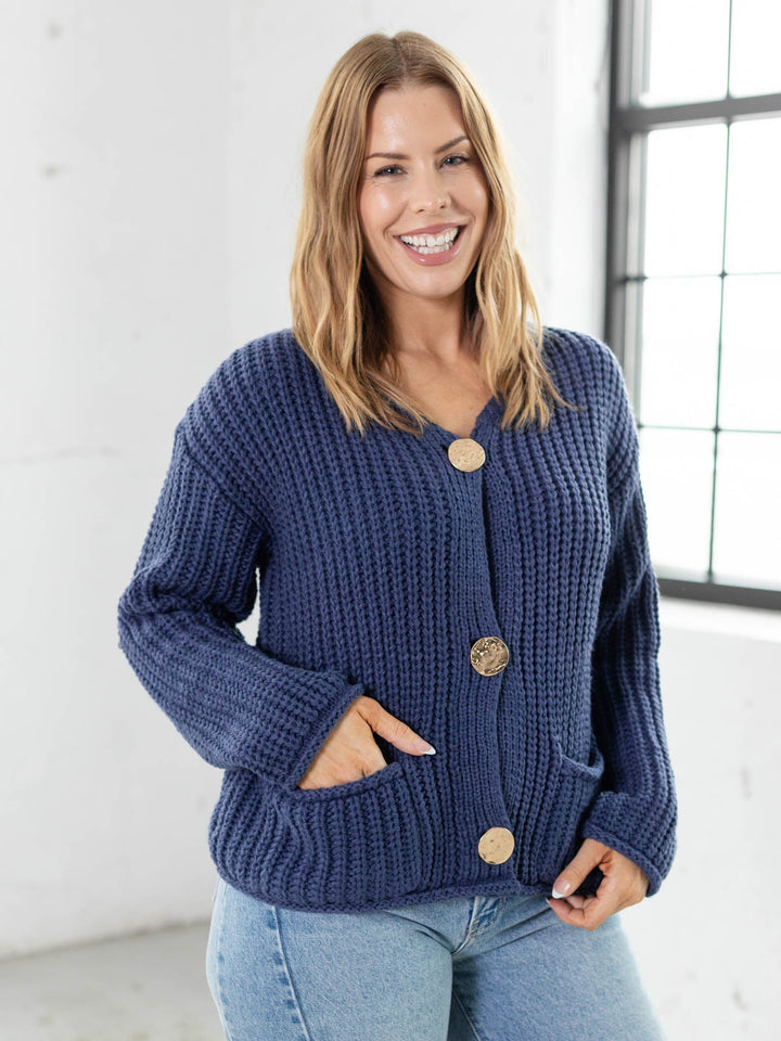 Woman wearing a blue knitted cardigan with gold buttons indoors.