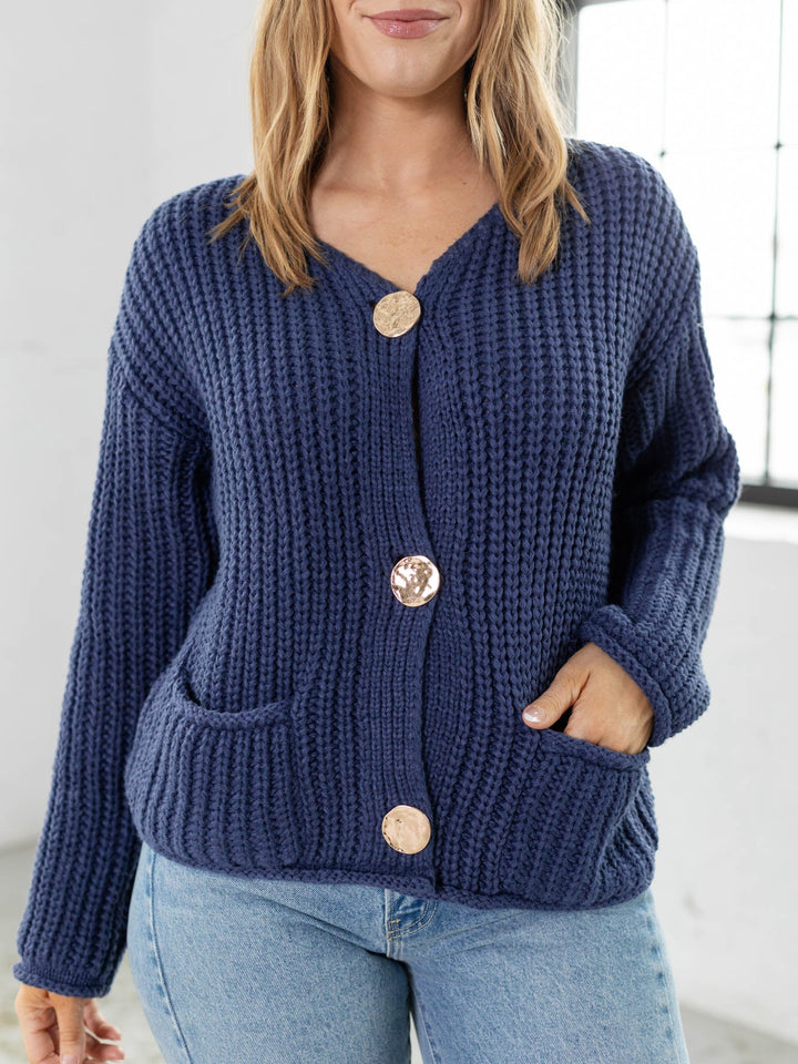 Woman wearing a blue knitted cardigan with gold buttons indoors.