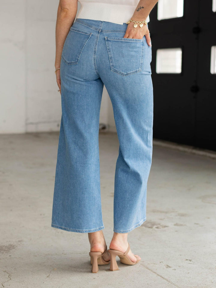 Person wearing light blue jeans standing in a minimal indoor setting.