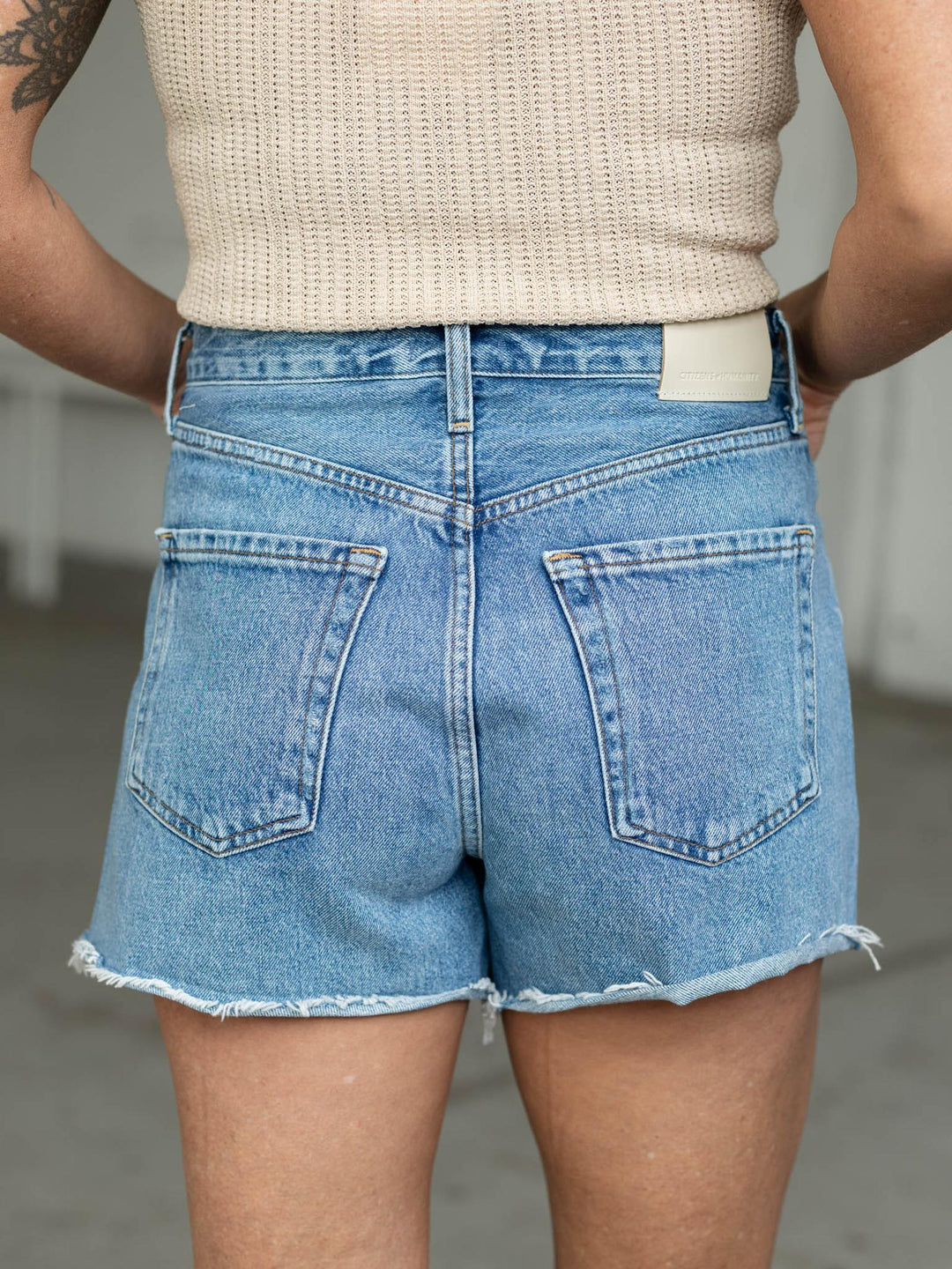 Person wearing blue denim shorts and a beige top with a neutral background