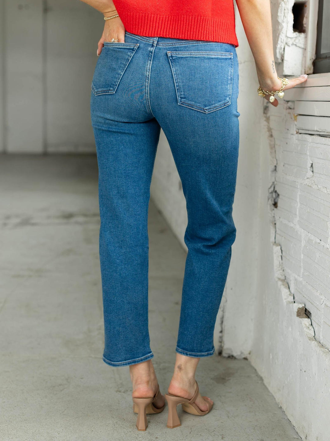 Person wearing blue jeans and a red top standing against a white wall.