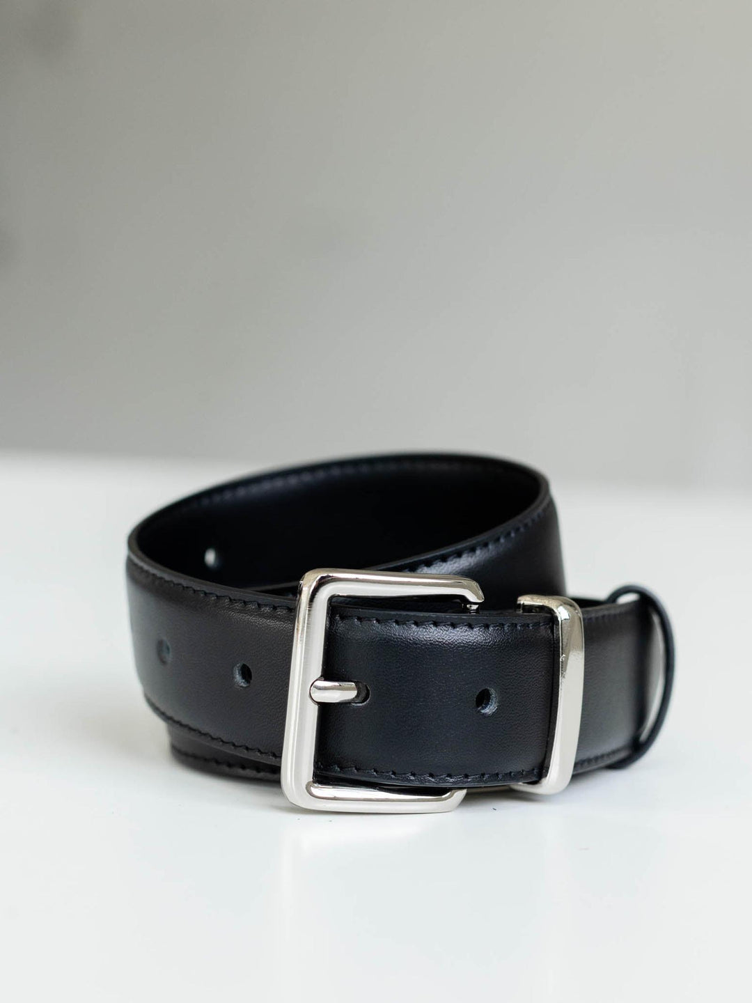Black leather belt with a silver soft echo-edge square buckle, coiled on a white surface.