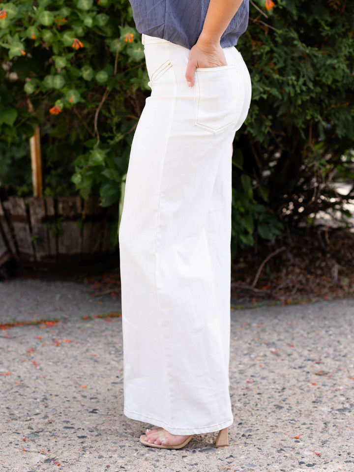Cream high waist flare pant with contrast top stitching, flap-over button waistband, and side pocket detail.