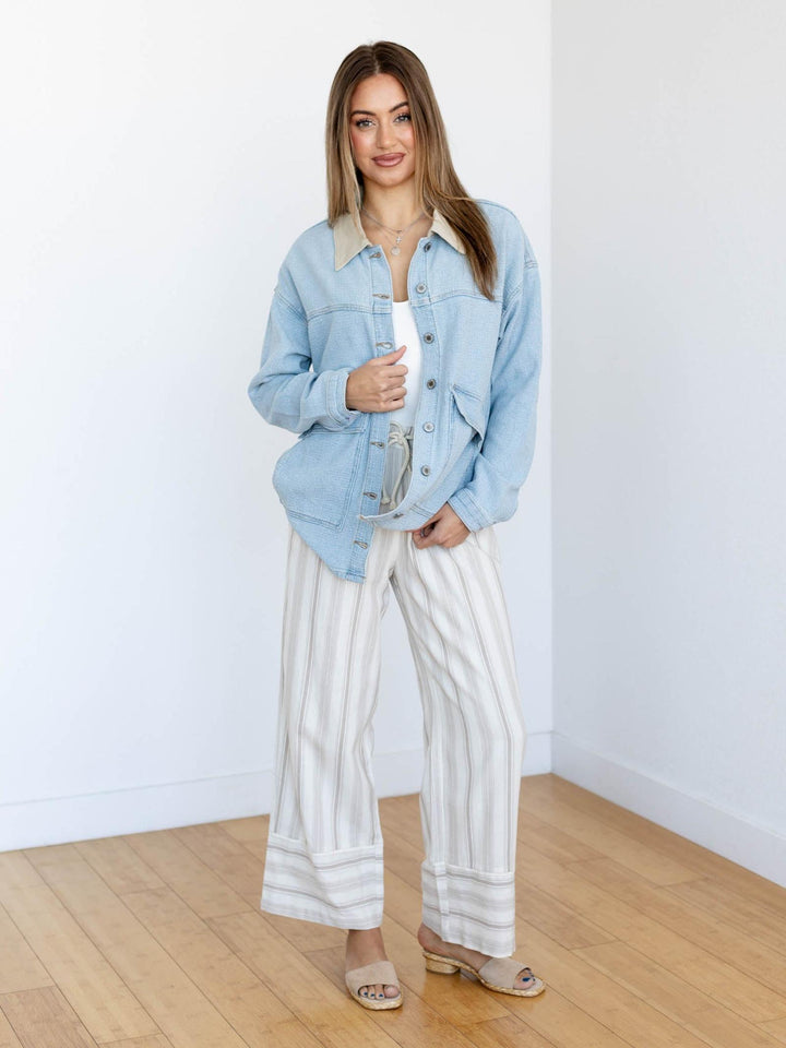 Woman wearing a light blue denim jacket and white striped pants in a minimal room.
