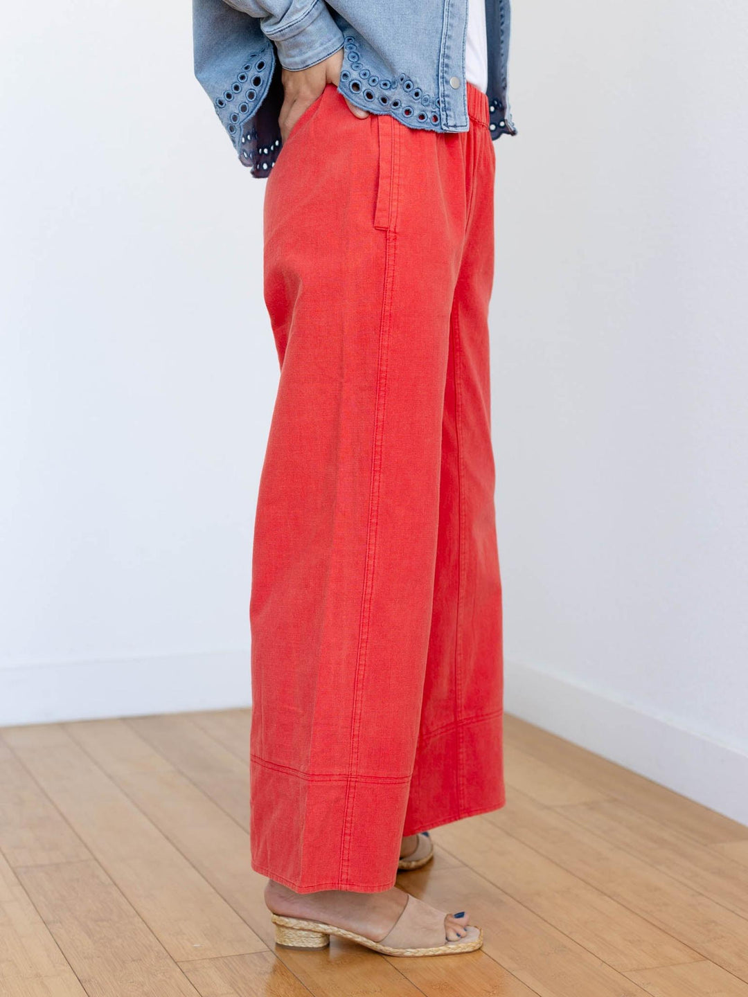 Person wearing red pants and a denim jacket on a wooden floor with a white wall background