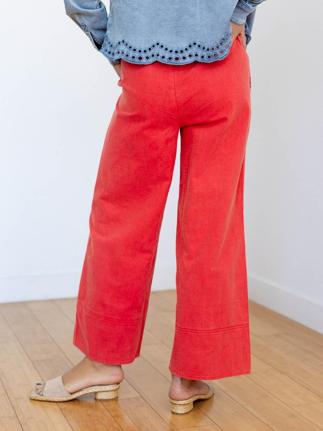 Person wearing red pants and a blue top on a wooden floor with a white wall background