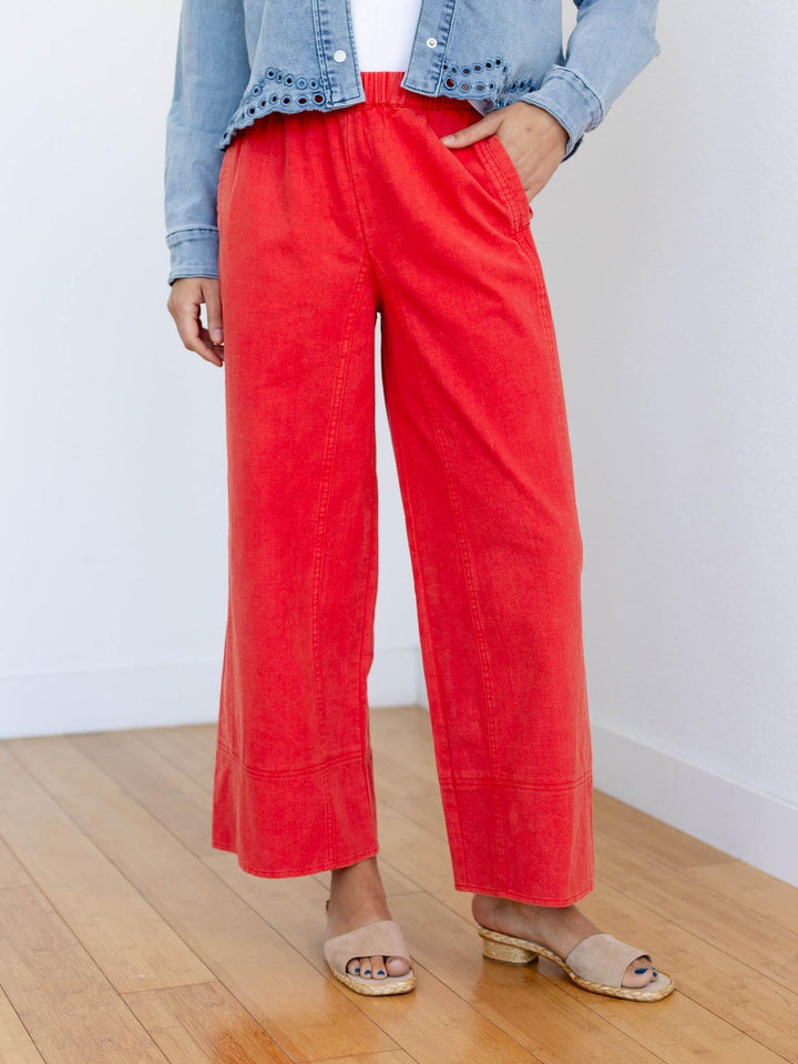 Person wearing red pants and a denim jacket on a wooden floor with a white wall background