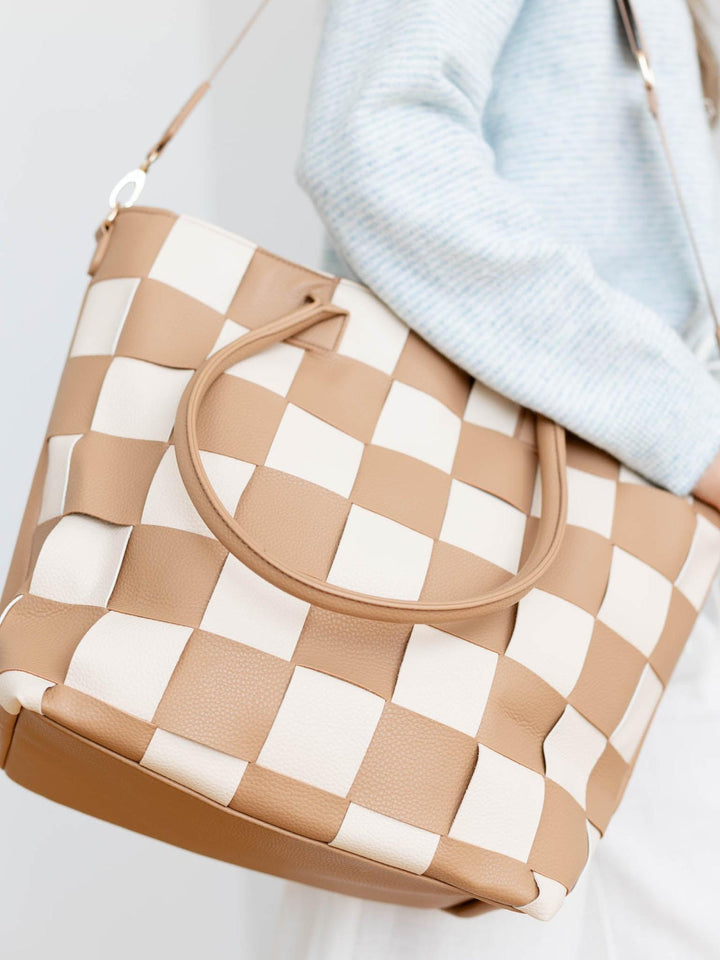Beige and white checkered handbag held by a person wearing a light blue sweater.