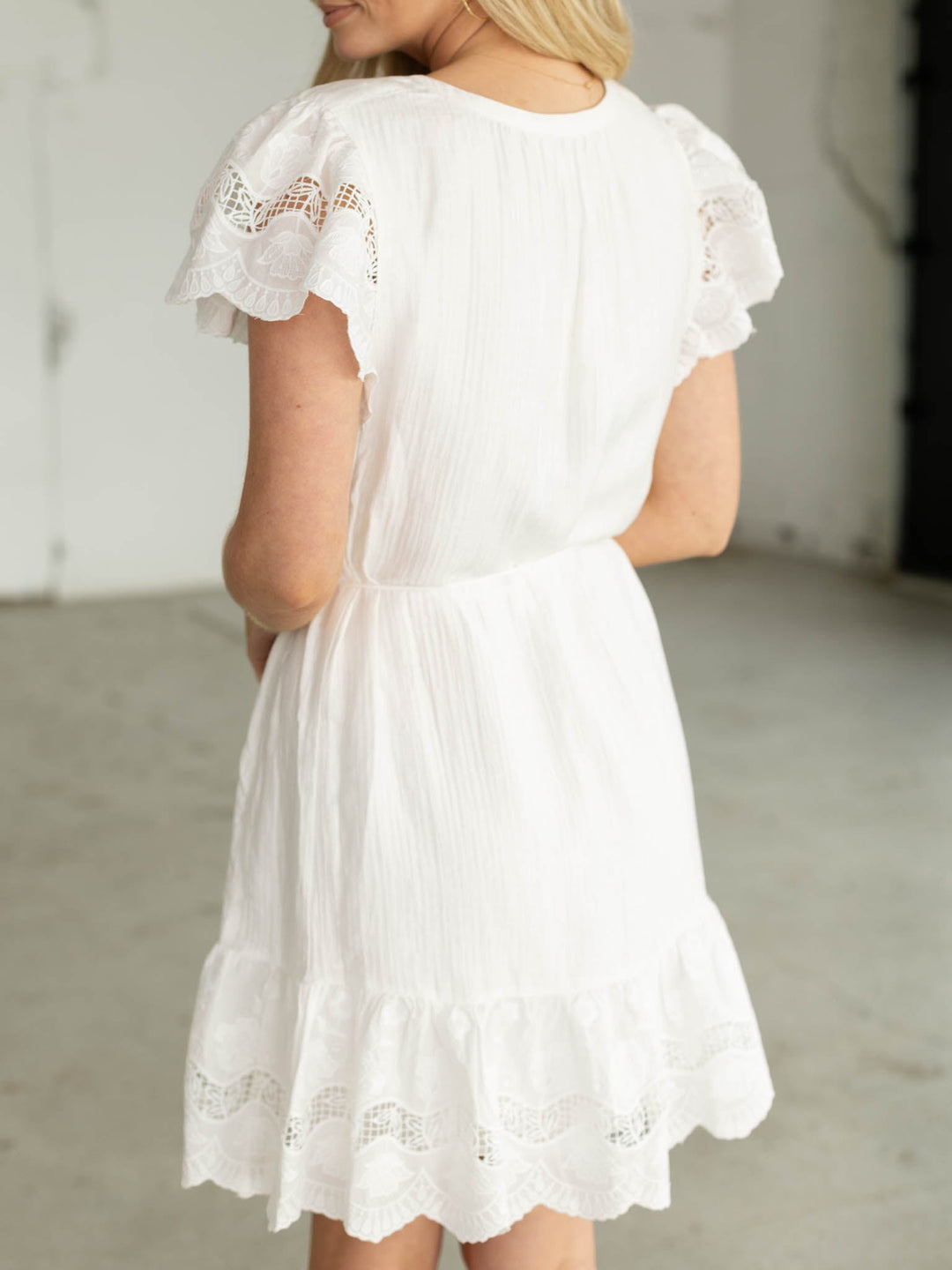 White dress with lace details worn by a person, against a neutral background