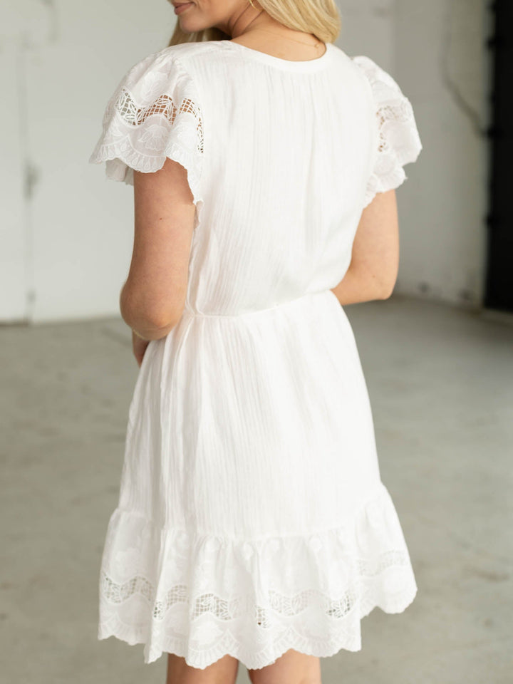 White dress with lace details worn by a person, against a neutral background