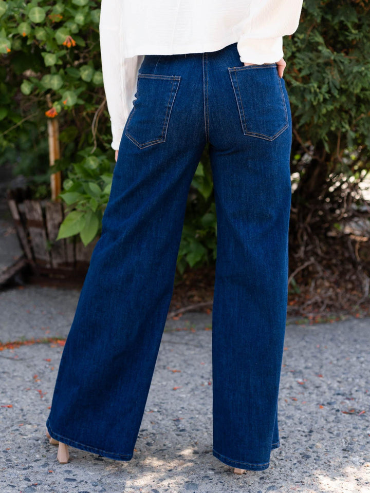 Dark wash denim high-waisted wide-leg jeans with back pockets and a flap-over button waistband.