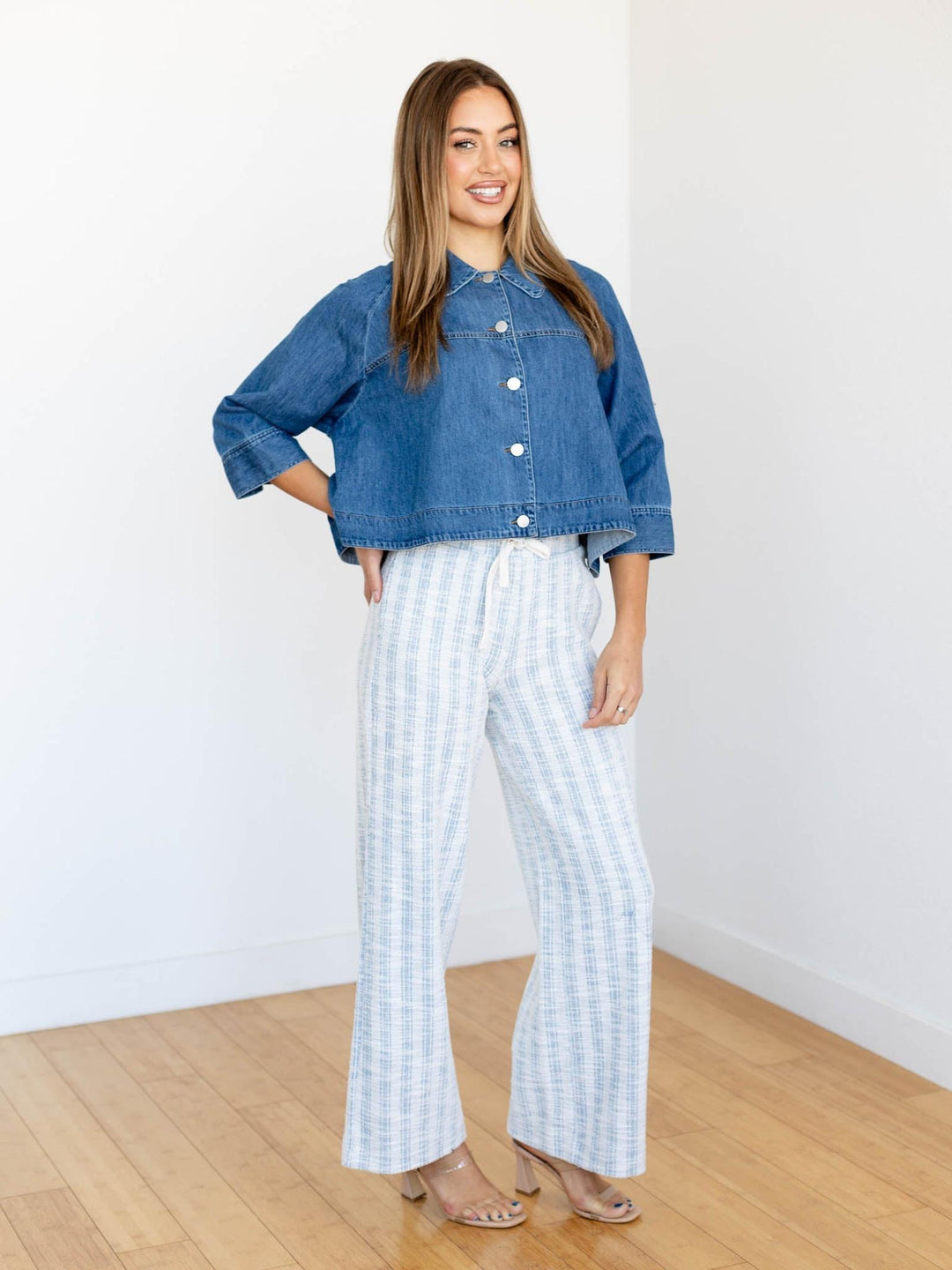 Woman wearing a blue denim jacket and white checkered pants standing in a room with wooden flooring.