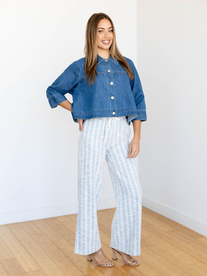Woman wearing a blue denim jacket and white checkered pants standing in a room with wooden flooring.