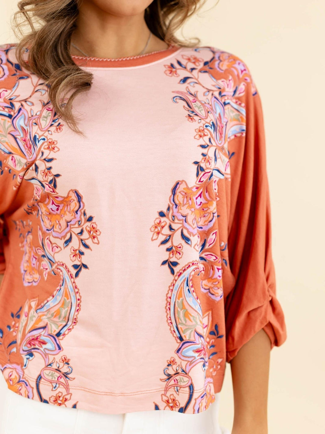 Coral floral patterned top worn by a person on a beige background