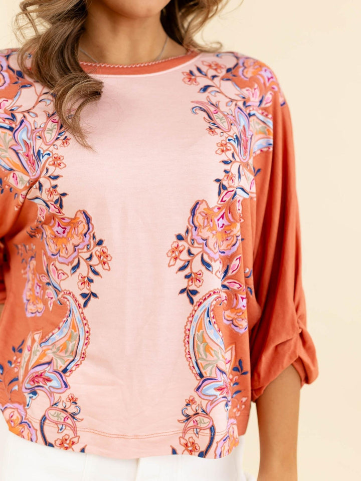 Coral floral patterned top worn by a person on a beige background
