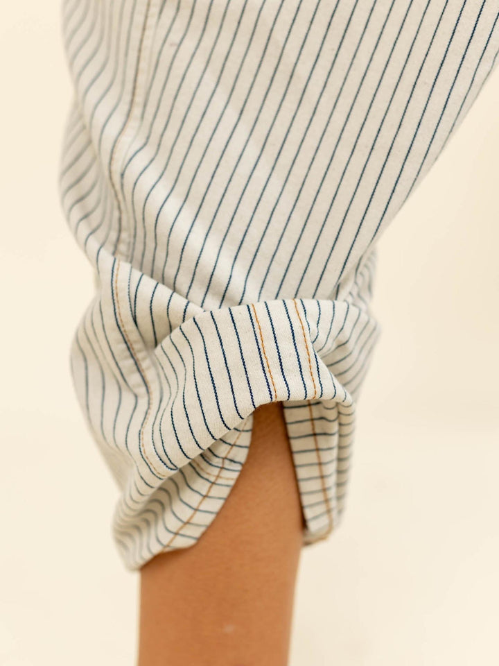 Close-up of a person wearing a striped shirt with rolled-up sleeves on a beige background