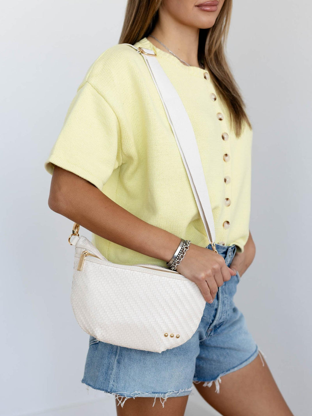 Person wearing a yellow shirt and denim shorts with a white quilted handbag on a plain background