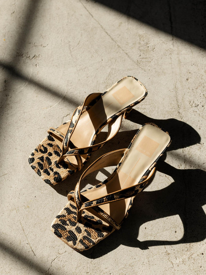 Pair of high-heeled sandals with leopard print soles on a textured surface