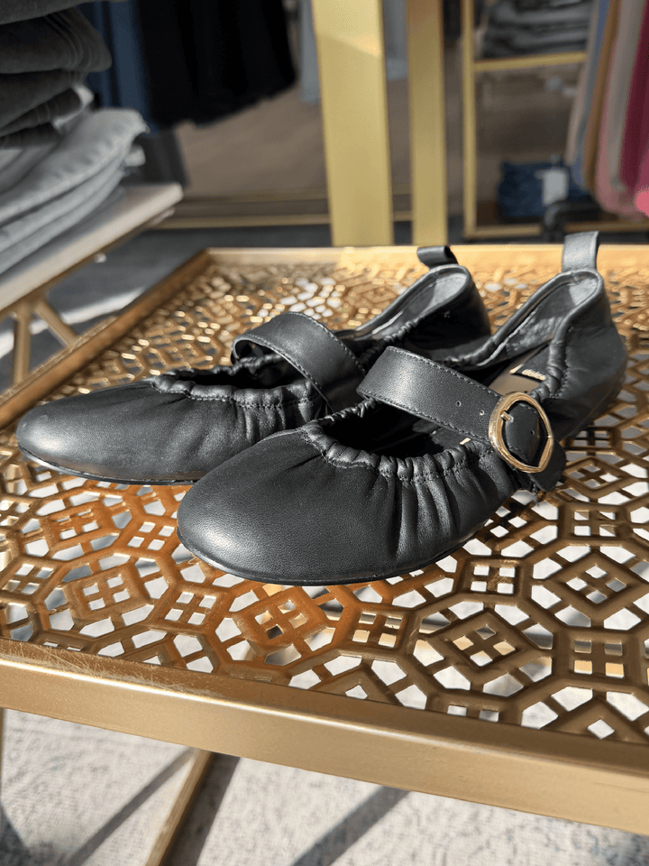 Black shoes with a gold buckle on a decorative wooden table