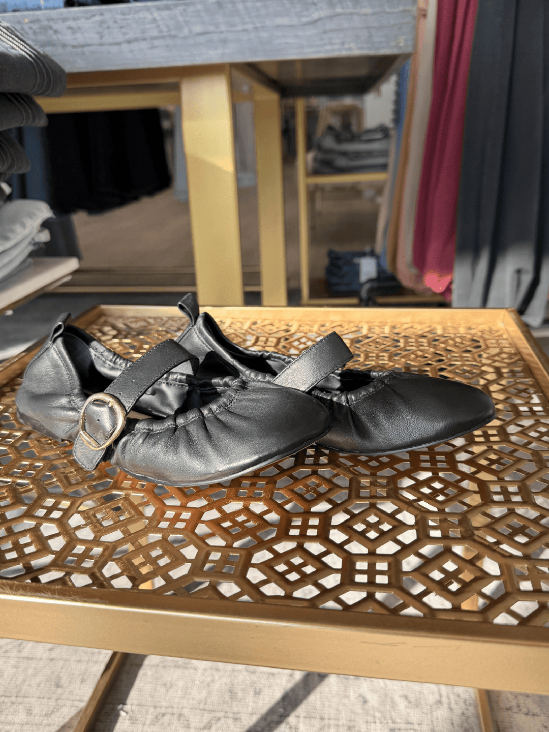 Pair of silver shoes with black straps on a decorative wooden table.