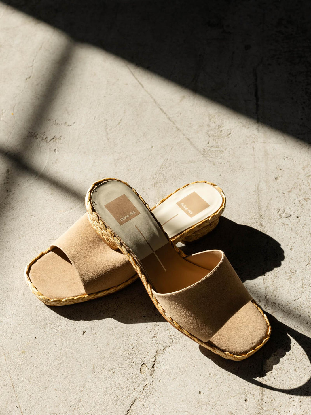 Pair of beige sandals on a textured surface with sunlight casting shadows.