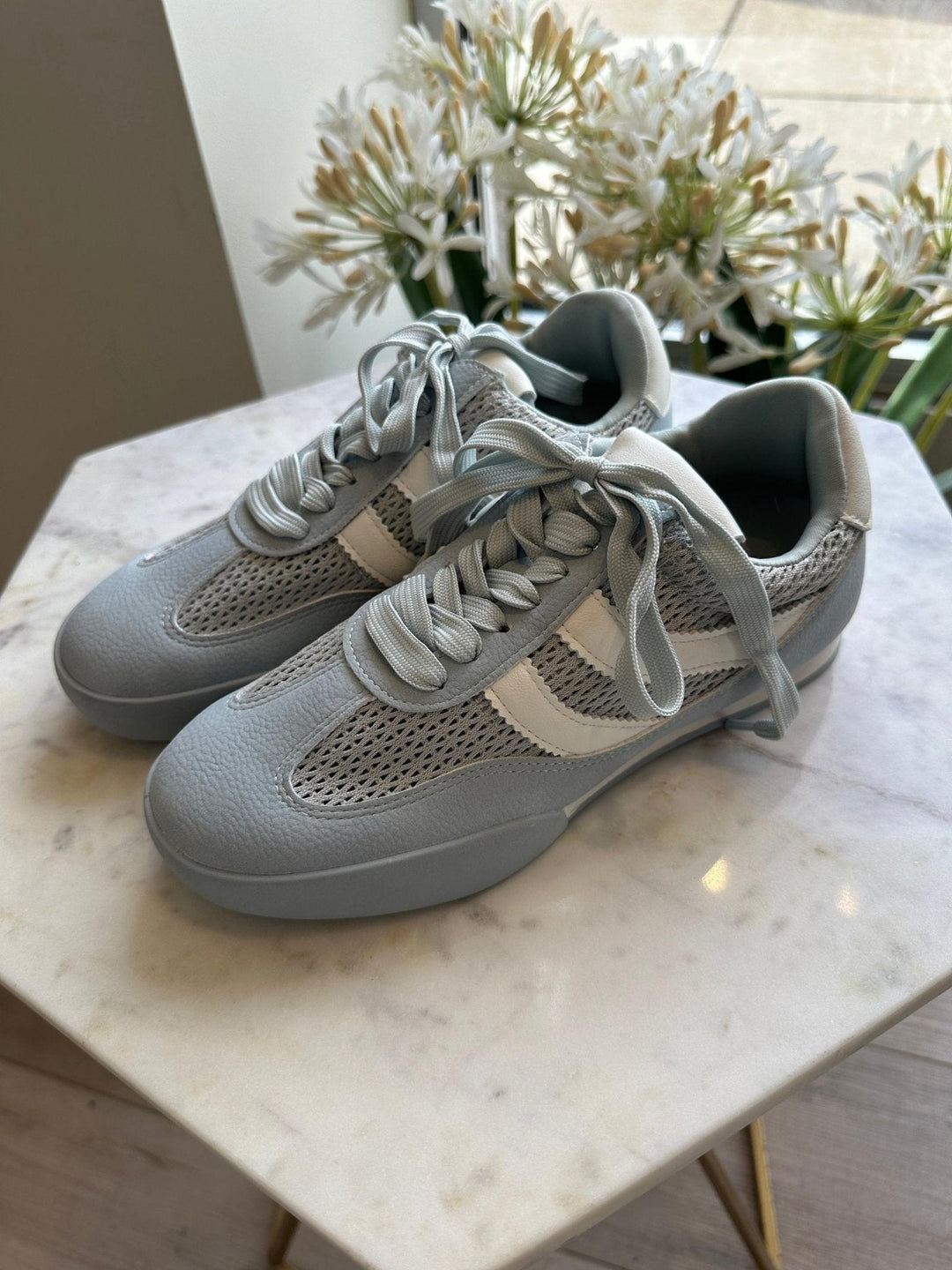 Pair of light gray sneakers on a marble surface with a plant in the background