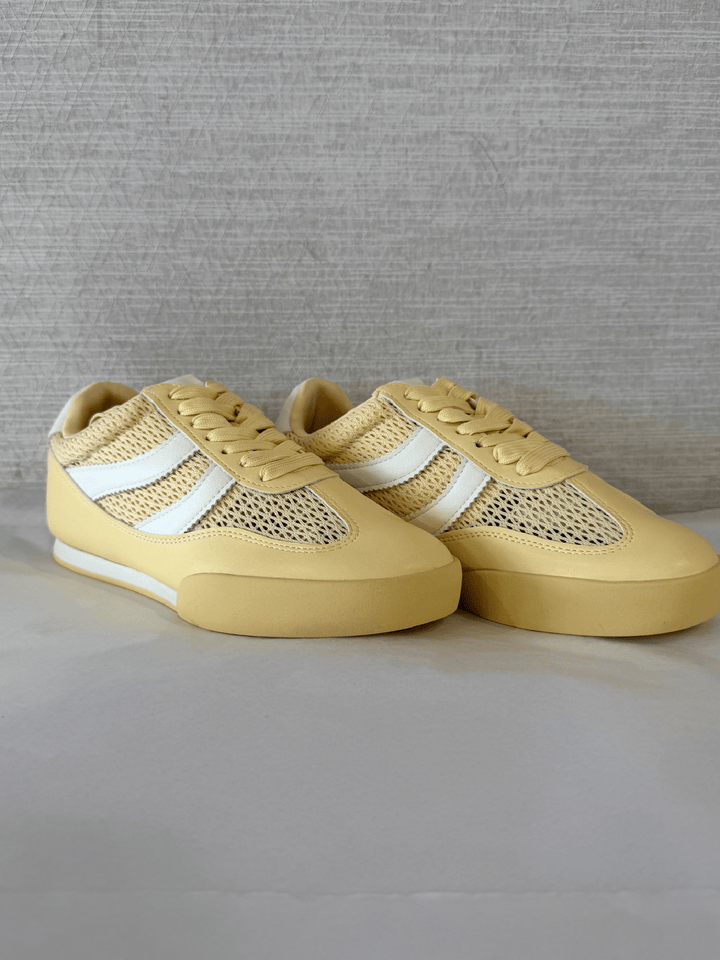 Pair of yellow sneakers with white accents on a gray background