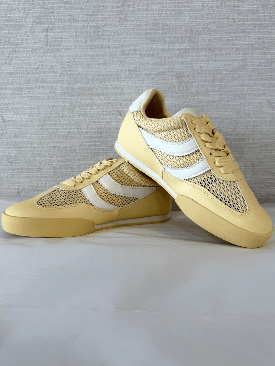 Pair of yellow sneakers with white accents on a light gray background