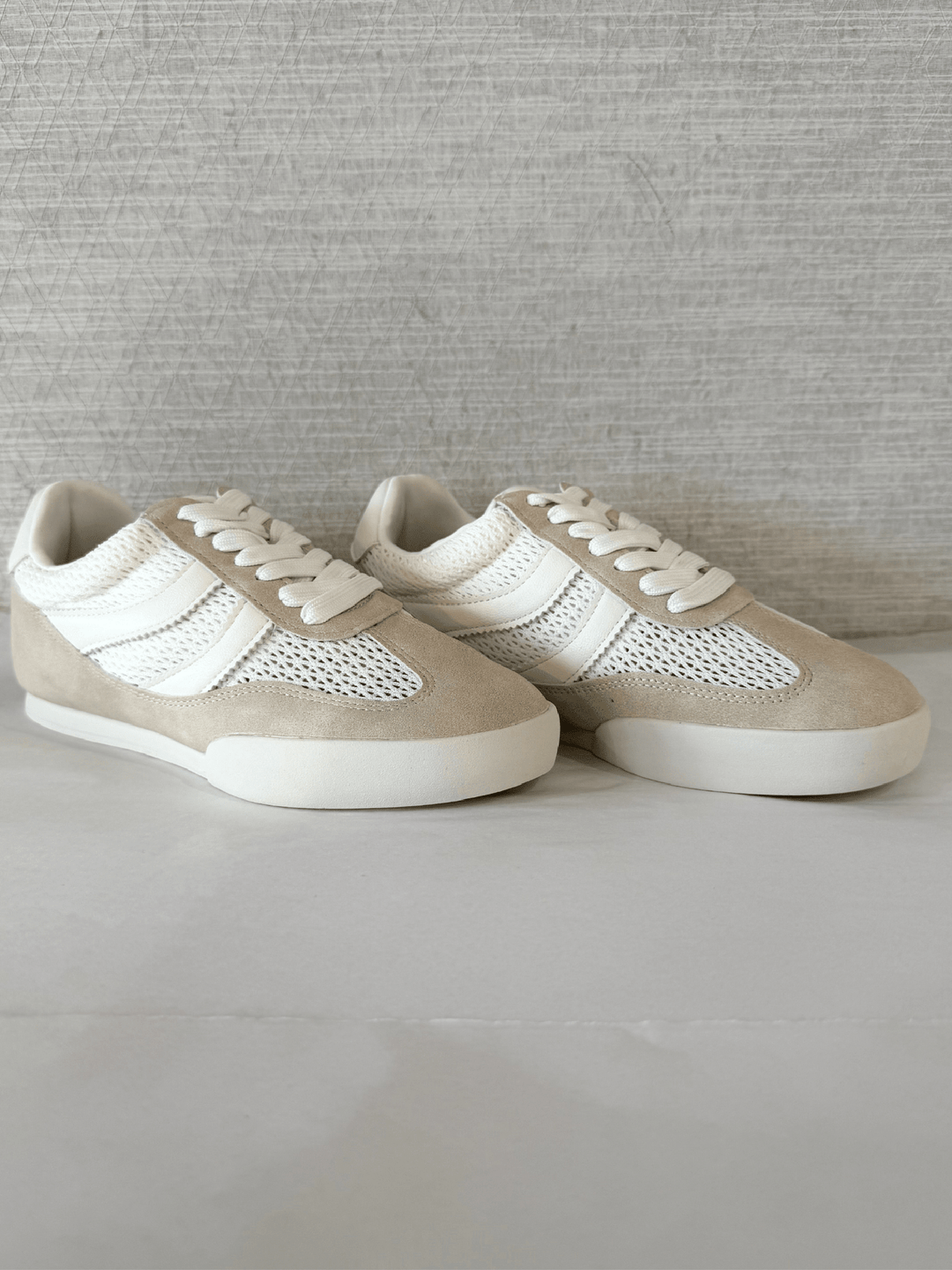 Pair of beige sneakers with white laces on a light gray surface.