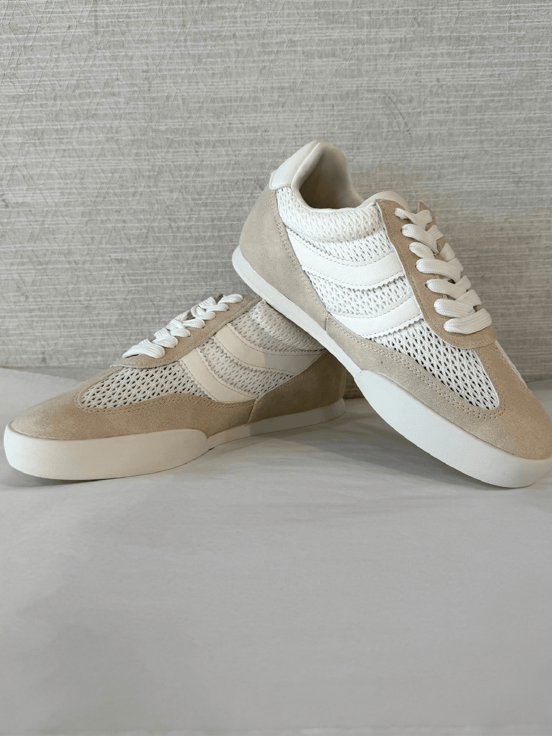 Pair of beige and white sneakers on a light gray surface with a neutral background