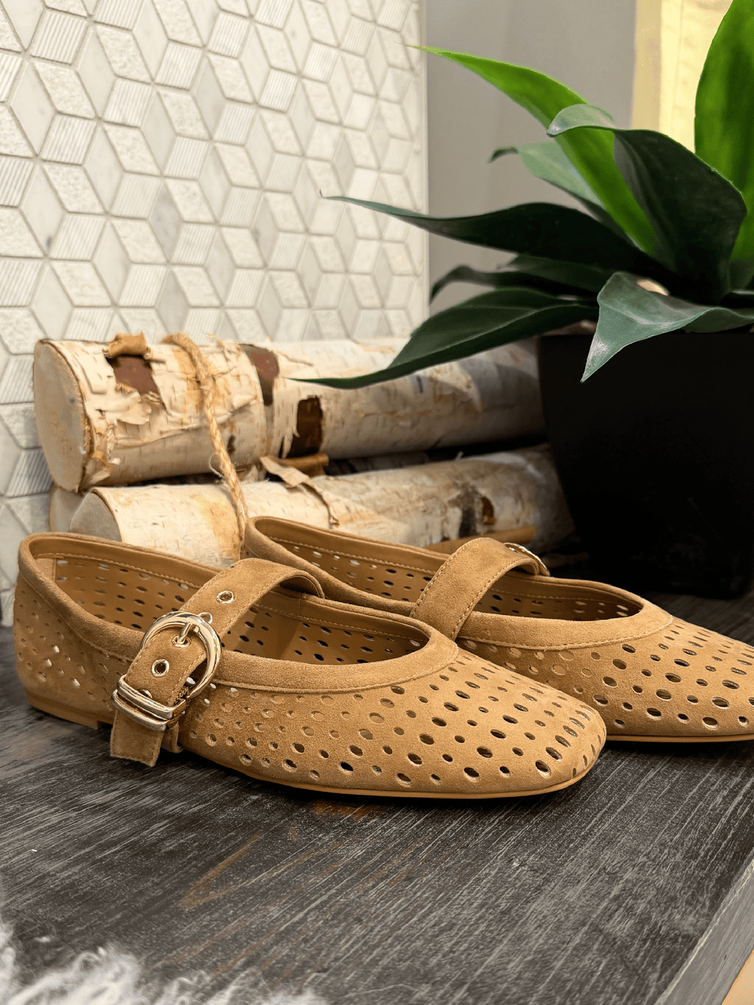 Tan shoes with a strap on a wooden surface with decorative elements in the background