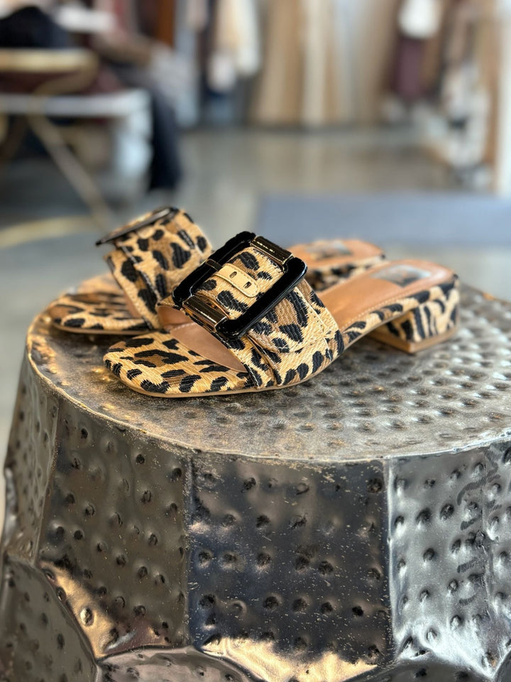 Leopard print sandals with a black buckle on a textured metallic surface.