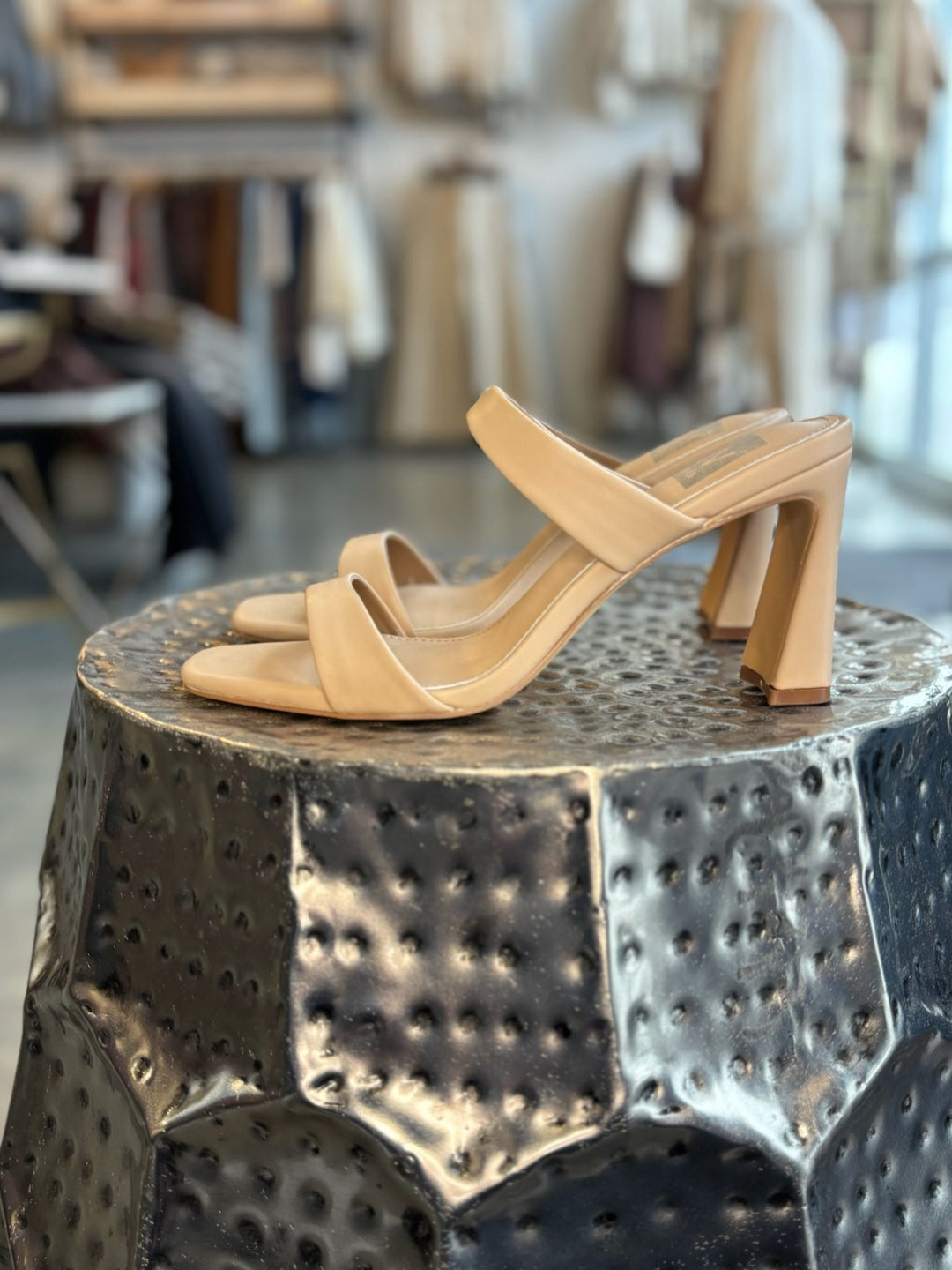 Tan high-heeled sandals on a metallic surface with a blurred indoor background