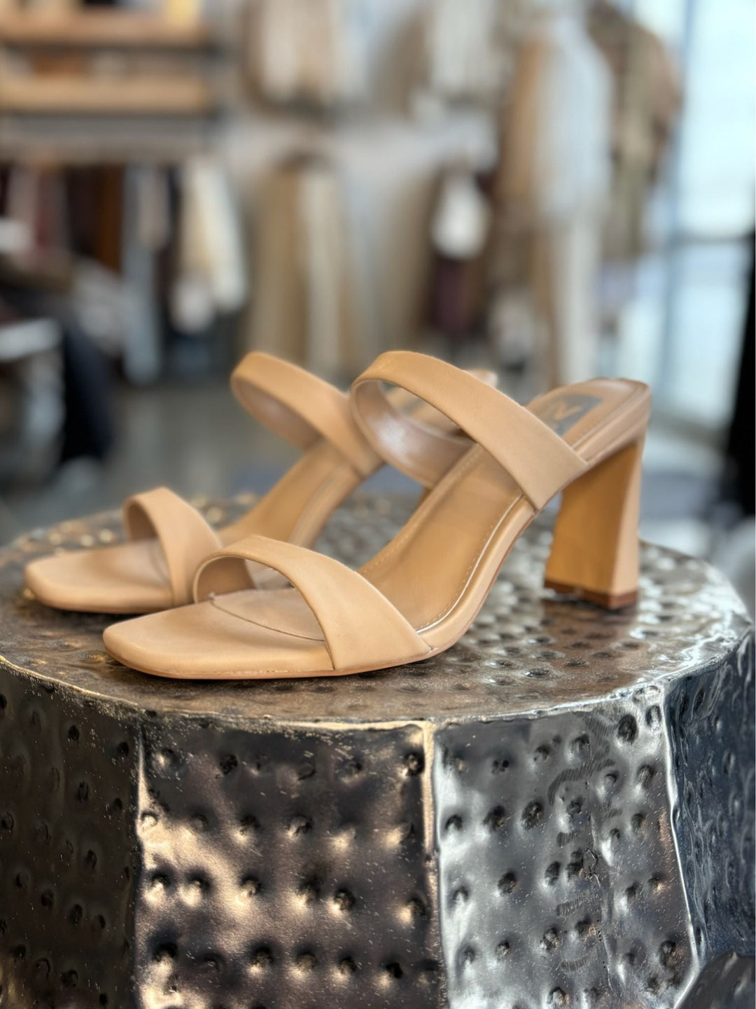 Tan high-heeled sandals on a metallic surface with a blurred indoor background