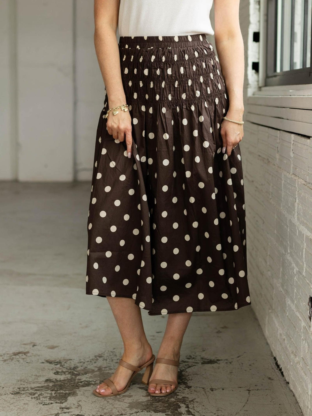 Person wearing a brown polka dot skirt standing against a neutral wall.