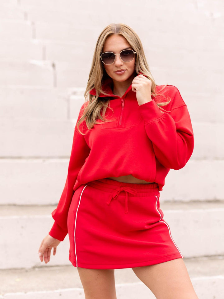 Woman in a red DoubleLUXE Piping Skort with white side piping, paired with a matching red sweatshirt.