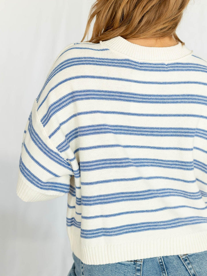 Person wearing a white and blue striped sweater with a plain background